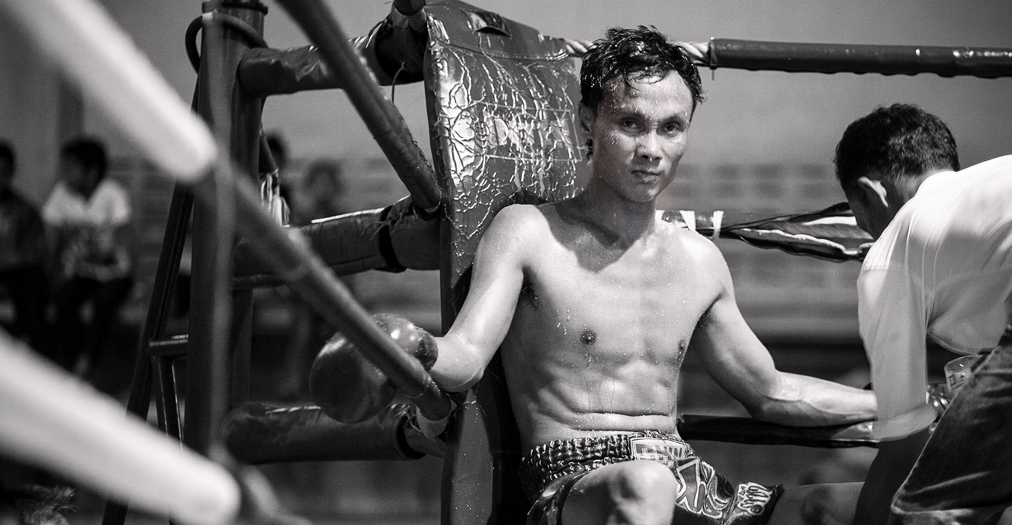 Thai boxer  with an aggressive expression sitting in a ring corner being prepped for his next round  